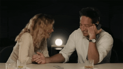 a man and a woman are sitting at a table talking on their cell phones