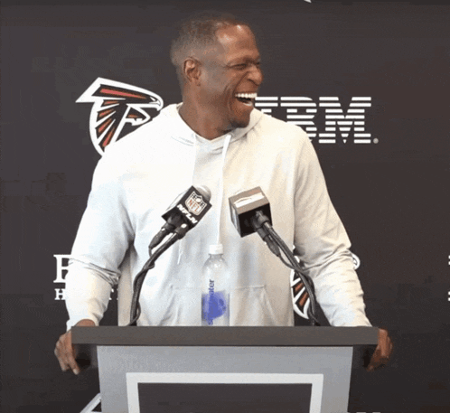 a man stands at a podium with microphones and a bottle of aquafina water