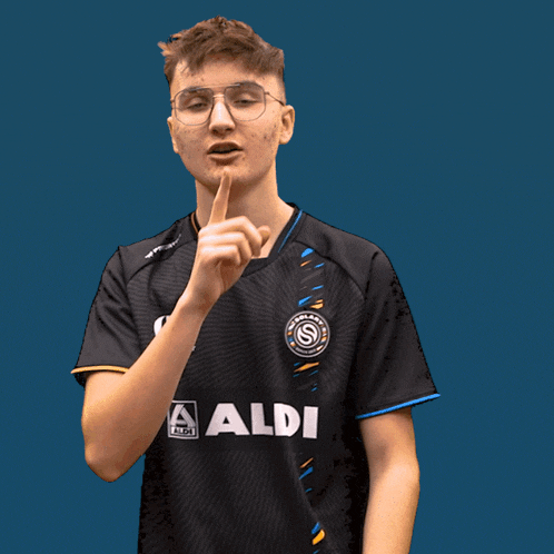 a man wearing a black aldi shirt holds his finger to his lips