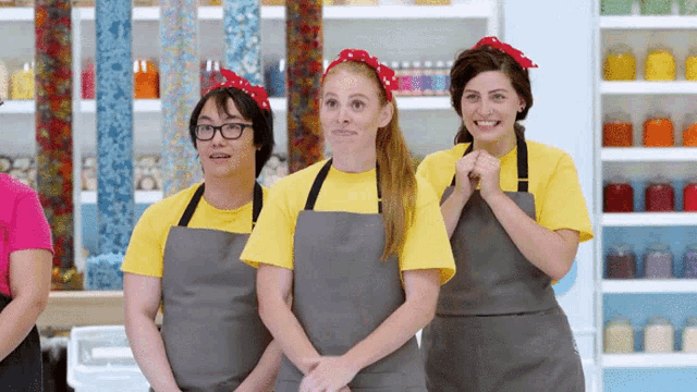 three people wearing aprons and yellow shirts are standing in a kitchen