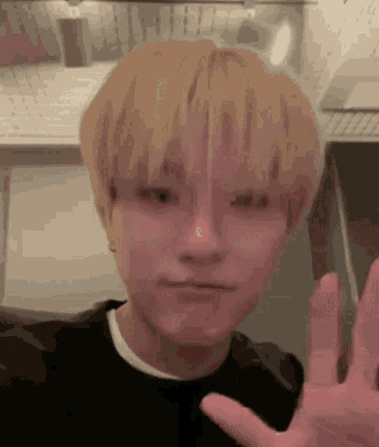 a young man with blonde hair is making a funny face with his hand out .