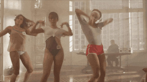 a group of women are dancing in a room with a man sitting at a table in the background