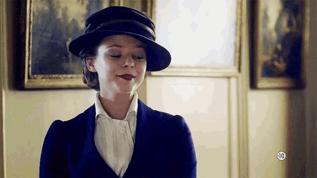 a woman wearing a hat and a suit is standing in a room with paintings .