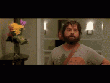 a man with a beard is standing in front of a vase of flowers on a table