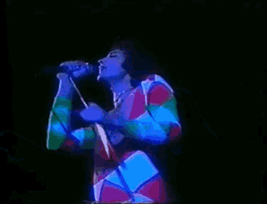 a man in a colorful outfit is singing into a microphone on a stage .