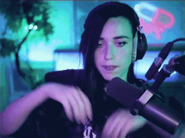 a woman wearing headphones stands in front of a microphone with a purple light behind her
