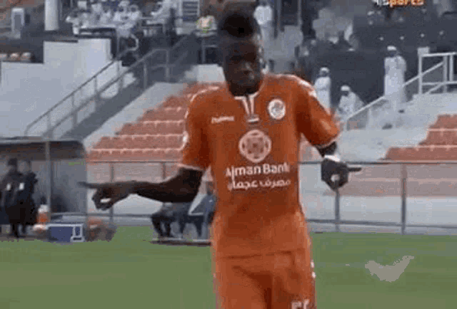 a soccer player is pointing at something on the field while wearing an orange jersey .
