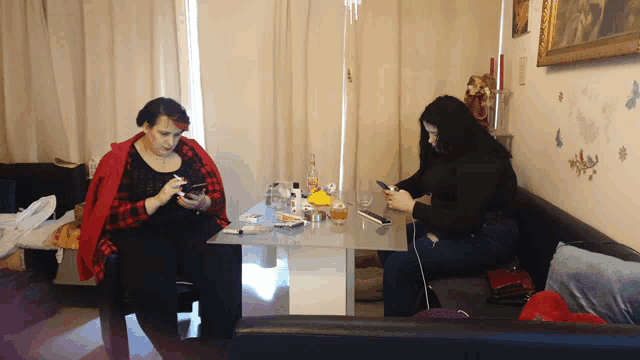 two women sitting at a table looking at their cell phones