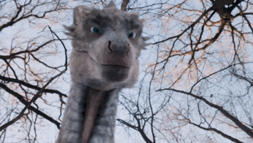 a stuffed animal that looks like a dragon is standing in front of a tree