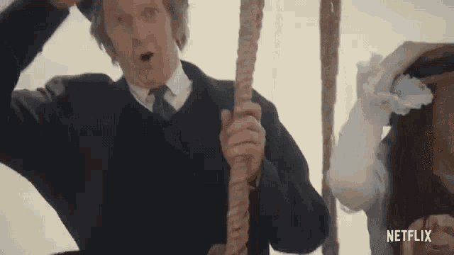 a man in a suit and tie is holding a rope in front of a woman in a white dress .