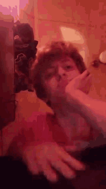 a man in a pink shirt is covering his mouth with his hand in a bathroom .