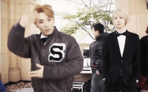 a man in a jacket with the letter s on it is standing next to another man in a suit .