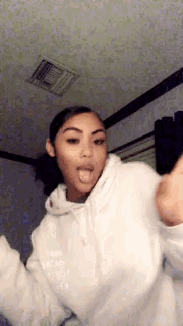 a woman in a white hoodie is making a funny face in a room .