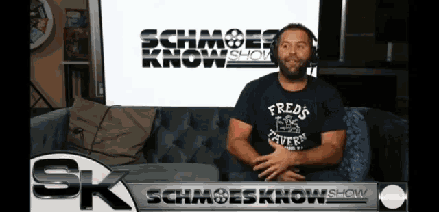 a man sits on a couch in front of a sign that says schmoes know show