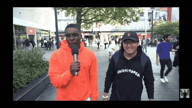 a man in an orange hoodie is holding a microphone and talking to another man