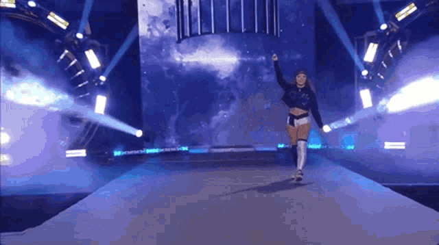 a woman is walking down a stage with her hand up in the air .