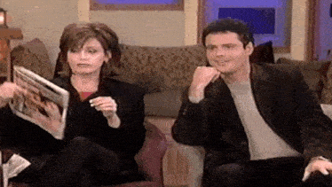 a man and woman are sitting on a couch reading magazines