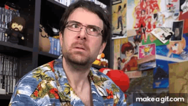 a man wearing glasses and a hawaiian shirt is sitting in front of a wall filled with posters .