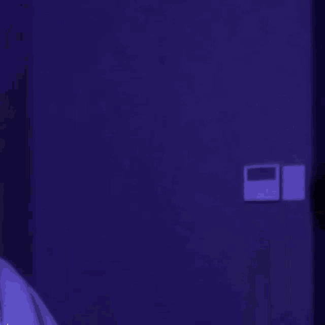 a person is standing in a dark room with a purple wall behind them .