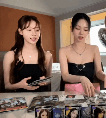 two women are sitting at a table looking at cards and one of them is wearing a necklace