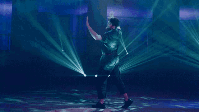 a man in a black shirt is dancing in front of a blue light