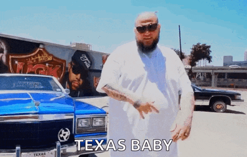 a man with a beard and sunglasses is standing in front of a blue car that says texas baby