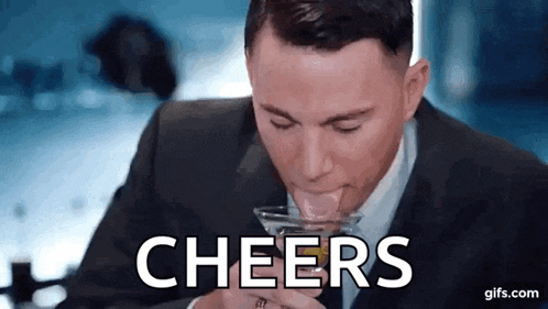 a man in a suit is drinking a martini from a glass with the word cheers written on it .