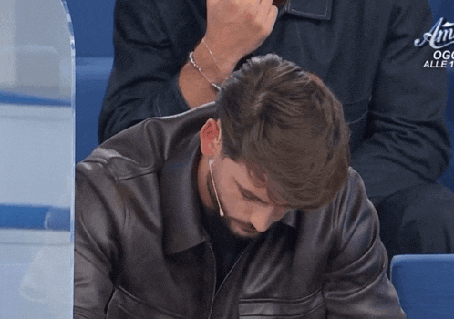 a man wearing a leather jacket is sitting in front of a sign that says " alle 1 "