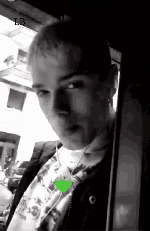 a black and white photo of a man wearing headphones and a green heart necklace .