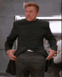 a man in a black suit is taking off his jacket and pants