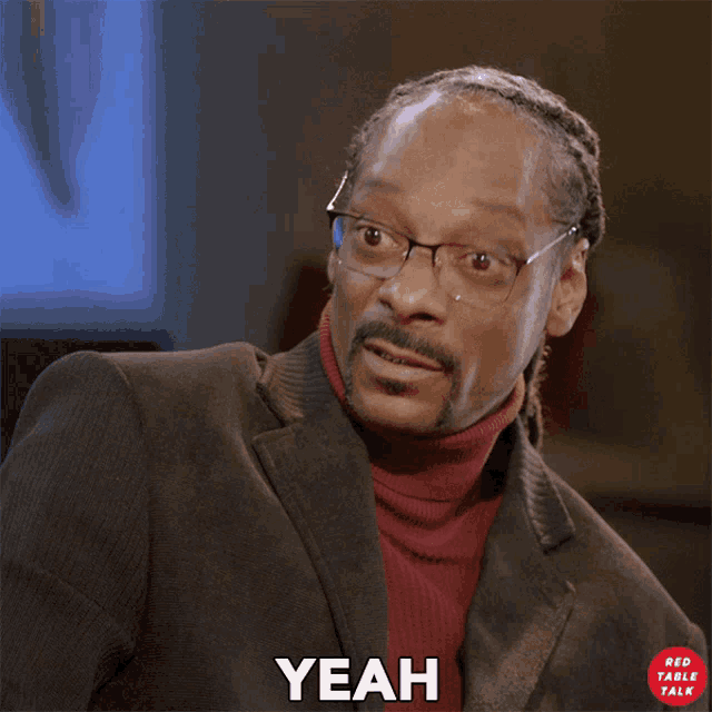 a man wearing glasses and a red turtleneck says " yeah "