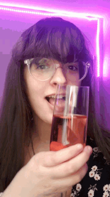 a woman with glasses is holding a glass of red liquid