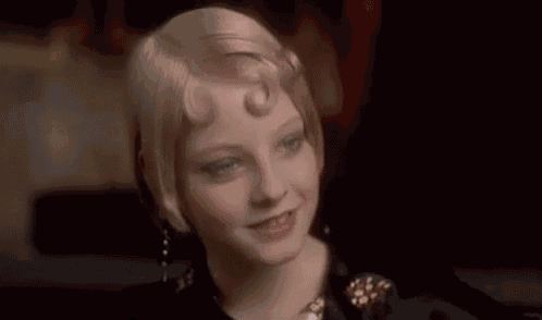 a woman is talking about smearing her lipstick while wearing a wig and earrings .