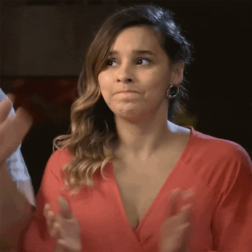 a woman in a red top is clapping her hands and making a funny face