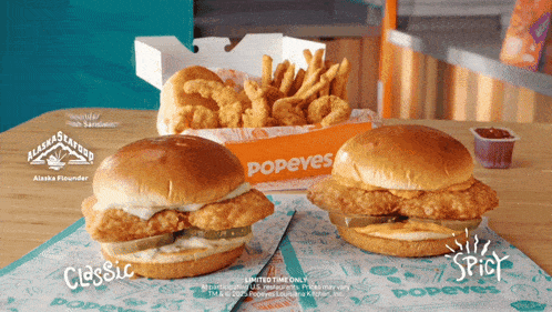 two popeye 's chicken sandwiches sit on a table next to a box of chicken nuggets
