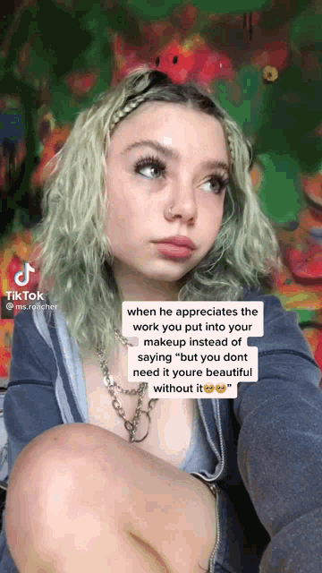 a girl with green hair is sitting in front of a painting and has a tiktok written on her face