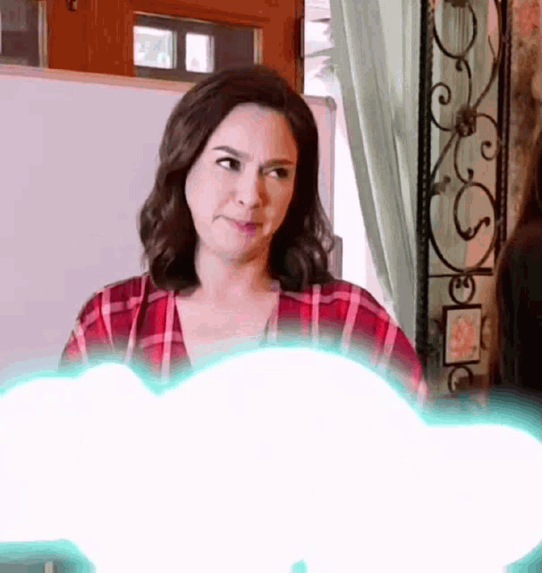 a woman in a plaid shirt is standing in front of a white board with a light coming out of it .