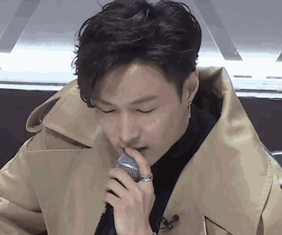 a man wearing a trench coat is holding a microphone in his hand