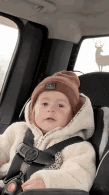 a little girl wearing a brown beanie and a white jacket is sitting in a car seat