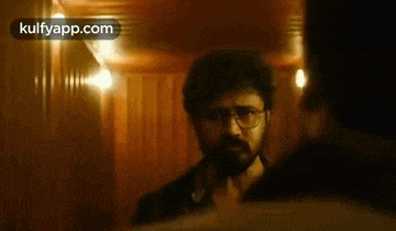 a man with glasses and a beard is standing next to another man in a hallway .