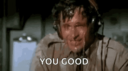 a man wearing headphones is sweating and saying `` you good '' while sitting on a plane .