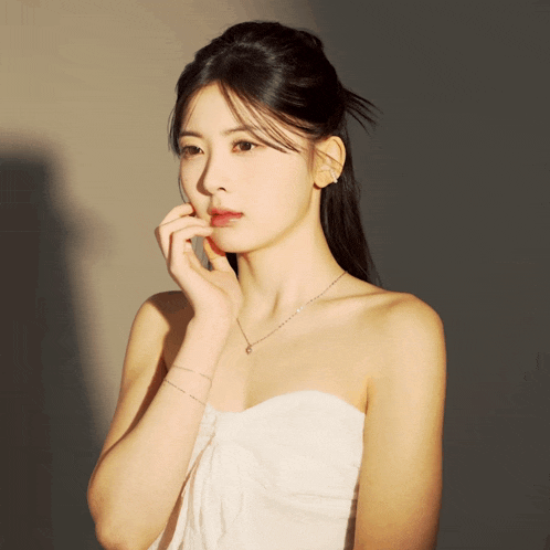 a woman in a white strapless dress is touching her face with her hand
