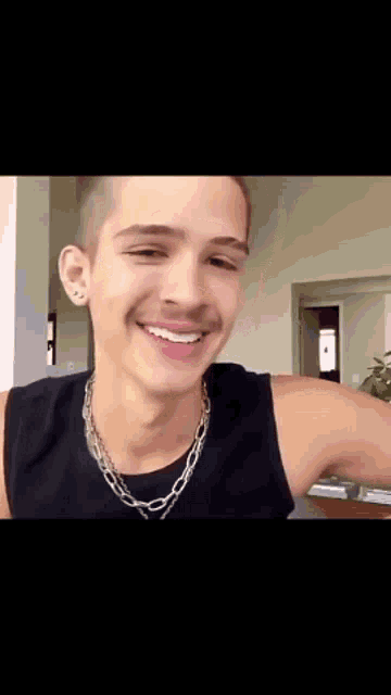 a man wearing a black tank top and a silver chain around his neck smiles