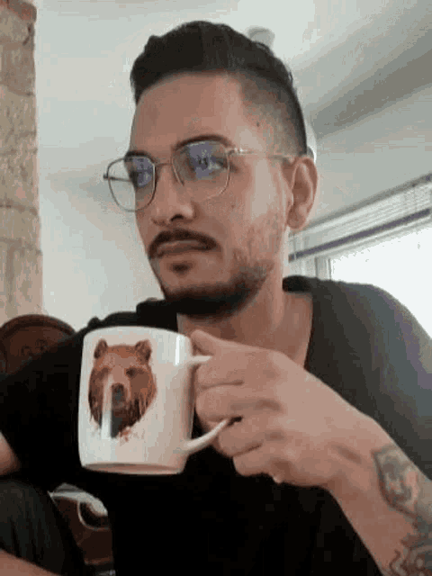 a man with glasses and a beard is holding a mug with a bear on it .