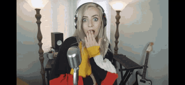 a woman wearing headphones is singing into a microphone and covering her mouth with her hand