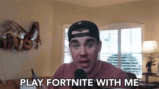 a man in a baseball cap is talking into a microphone while playing fortnite with me .