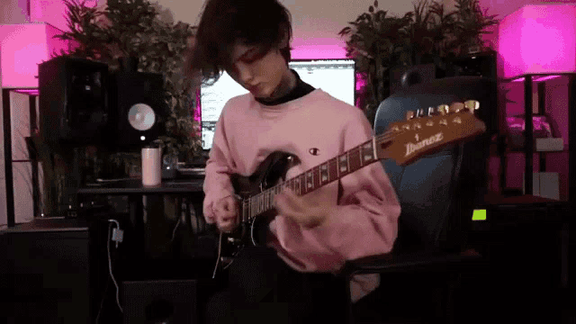 a person in a pink sweater is playing an ibanez electric guitar