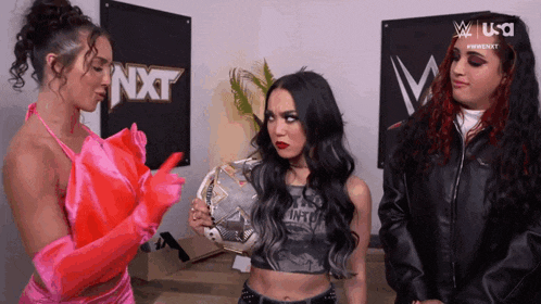 three women are standing in front of a sign that says nxt on it