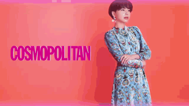 a woman in a blue dress is standing in front of a pink background with the word cosmopolitan .