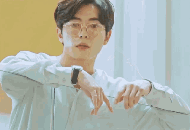 a young man wearing glasses and a watch leans on a glass railing